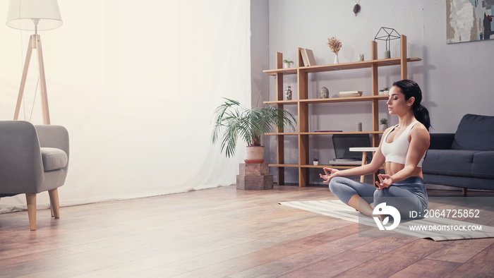 Side view of young woman meditating in living room