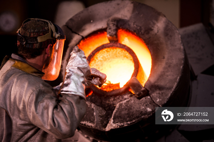 Steel worker in protective clothing raking furnace in an industr