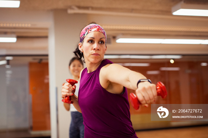 Confident female athletes holding dumbbells while exercising in gym