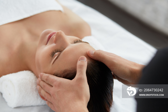 Young beautiful woman enjoying anti-aging facial massage.Male therapist making head massage to femal