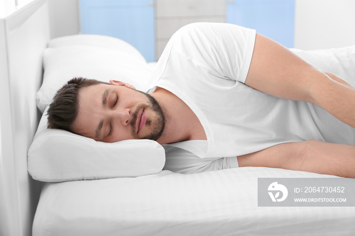 Young man lying on bed with orthopedic pillow at home