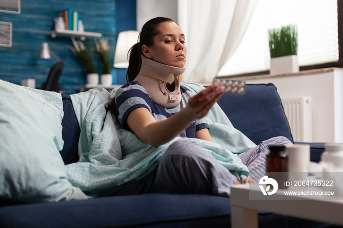 Woman in neck brace suffering from pain on sofa after bad accident injury. Young caucasian adult wit