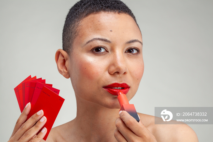 Studio portrait of woman applying red lipstick and holding color swatch