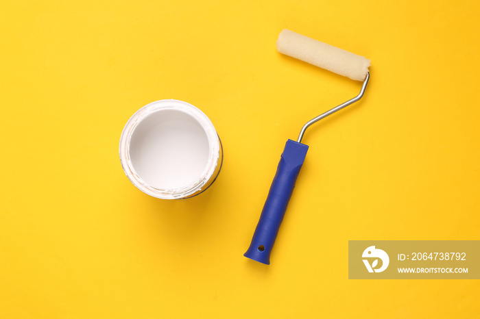 Paint roller and a can white paint on yellow background. Top view. Home renovation concept