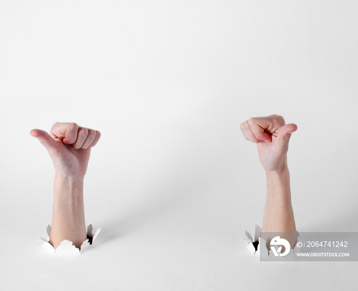 Female hands show thumbs up through the torn holes of white background. Creative art