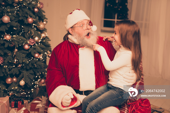 smart little girl sitting on the lap of old Santa and  pulling h