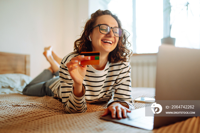 Online shopping аt home. A young woman holds a credit card and uses a laptop. Black friday, sale, co