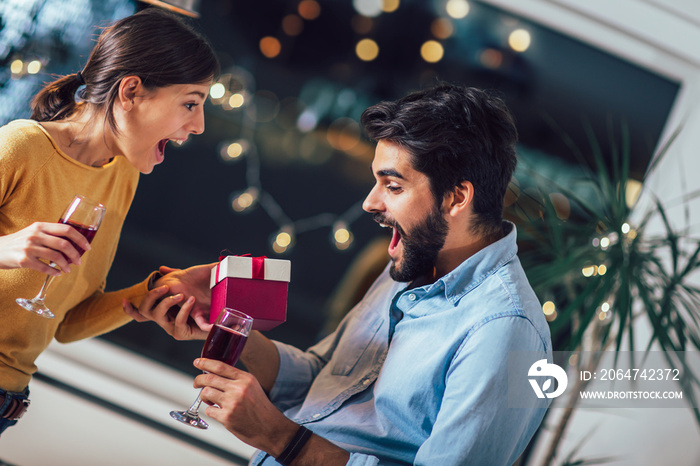 Beautiful young couple is celebrating at home. Pretty girl is giving her boyfriend a gift box