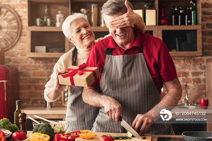 Excited senior woman giving gift to her loving husband at kitchen