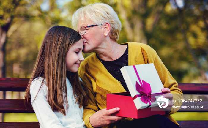 Grandchild surprised her grandmother with a birthday present in the park. Lifestyle, family concept