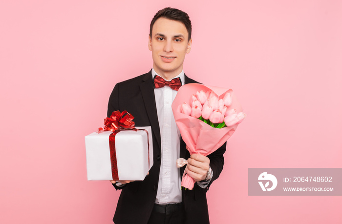 elegant man, in a suit, with a bouquet of flowers, and a gift box, on a pink background, the concept