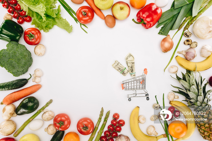 白色隔离的蔬菜和水果之间夹着美元的小型购物车俯视图