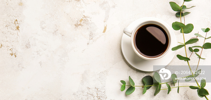 Cup of hot coffee and eucalyptus branch on light background