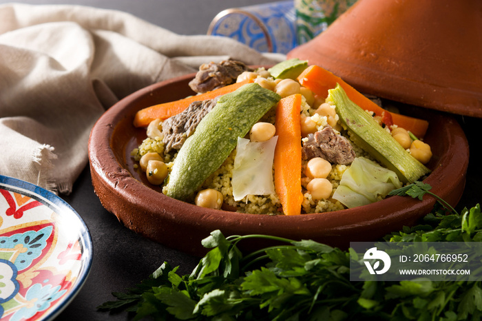 Traditional tajine with vegetables, chickpeas, meat and couscous on black slate