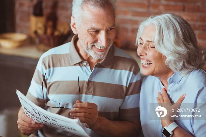Cheerful aged couple reading newspaper