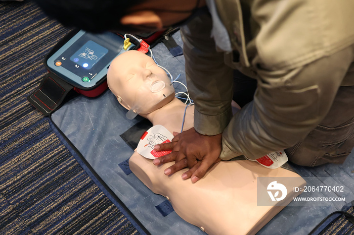 Asian man practicing CPR on a plastic mannequin with Automated External Defibrillator (AED) on the f