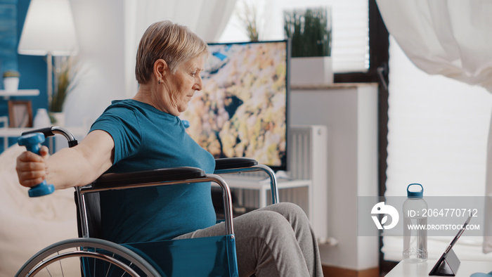 残疾老年妇女使用哑铃锻炼，并在数字平板电脑上观看锻炼视频。