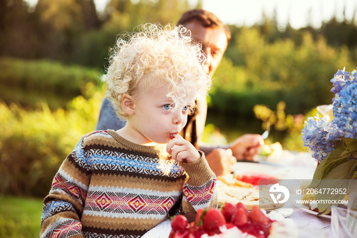 Portrait of girl (2-3) sitting at dining table outdoors with finger in mouth