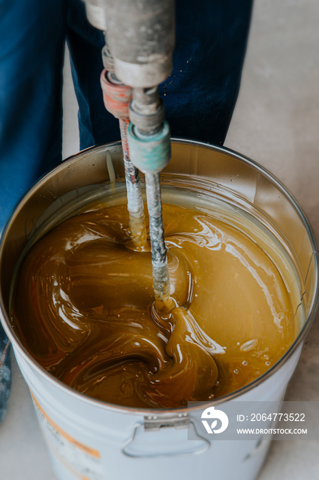 Worker mixing yellow epoxy resin with the mixer in a tin bucket