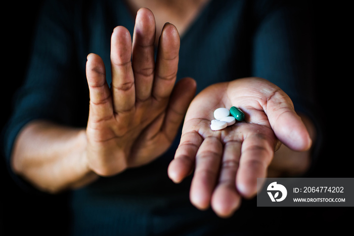 Close up hand of old woman holding a pill on black background, concept illness and healthcare