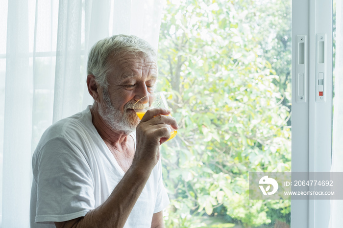 senior man hold glass of orange juice and thinking and looking outside of window in white room