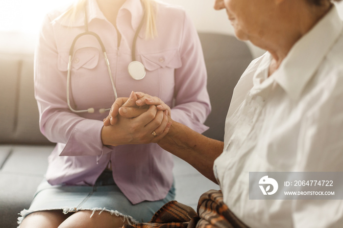 Young doctor holding hand of elderly woman on light background