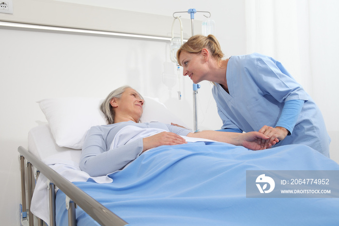 护士抚摸躺在医院病床上的老年妇女并握住她的手臂，安慰她