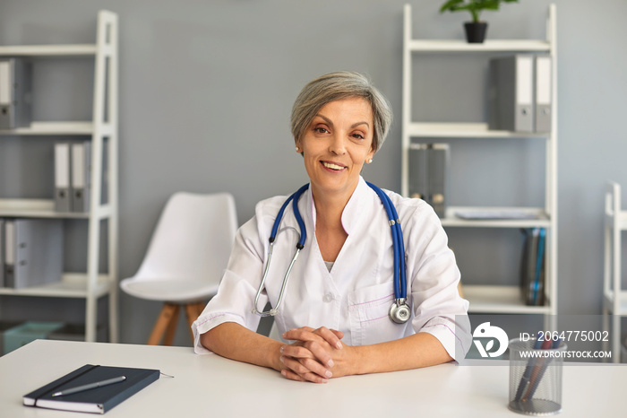 Mature doctor looking at camera, talking to patient online from office. Senior medical worker on web