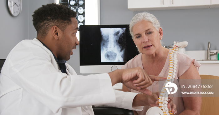 Portrait of young african-american doctor showing model of back spine to patient. Close up of senior