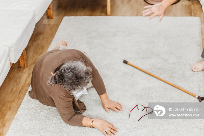 Asian senior woman falling down lying on floor at home and senior man hands try to help. Elderly wom