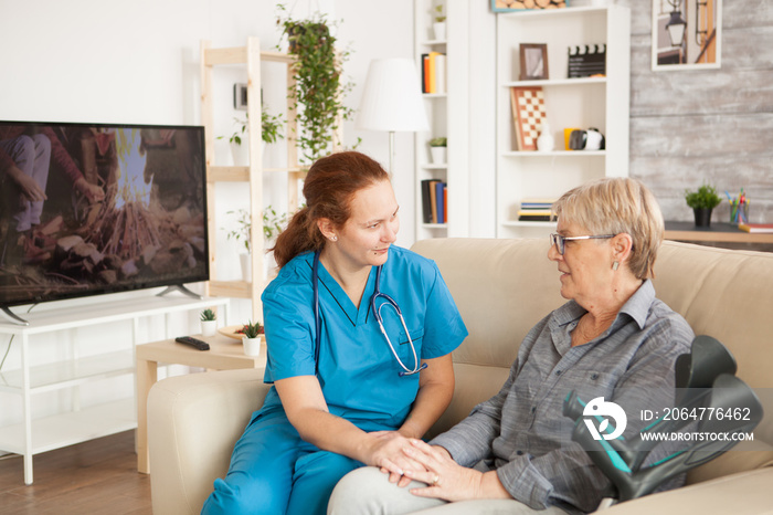 Female assistant talking with senior woman in nursing home with crutches.