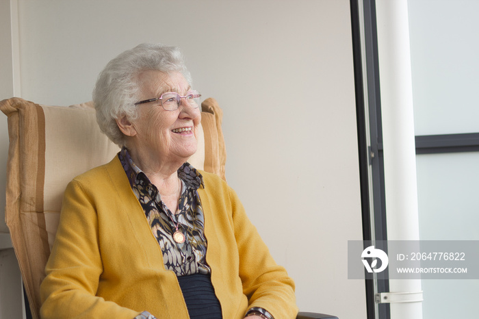 Horizontal portrait of an old senior woman, 80s adult, grandmother, sitting in a chair on her balcon