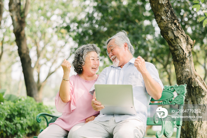 一对亚洲老年夫妇在公园里拿着笔记本电脑大笑