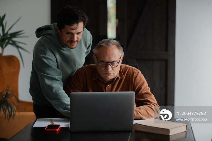 戴眼镜的老人和他的儿子在家里使用笔记本电脑。