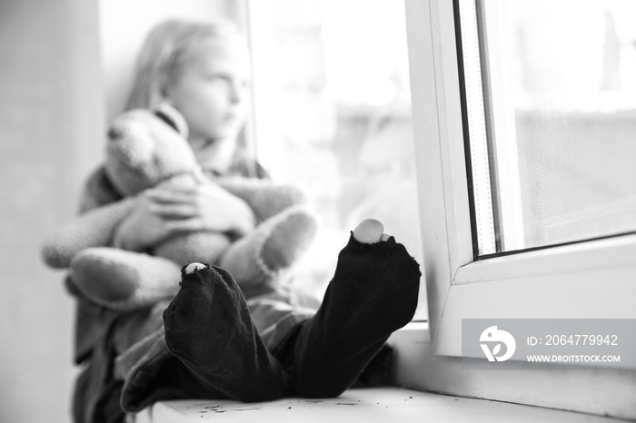 Homeless little girl sitting on window sill