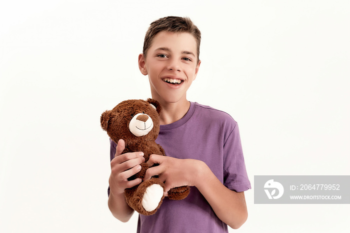 快乐的患有脑瘫的十几岁残疾男孩的肖像，对着镜头微笑，抱着他的泰迪熊