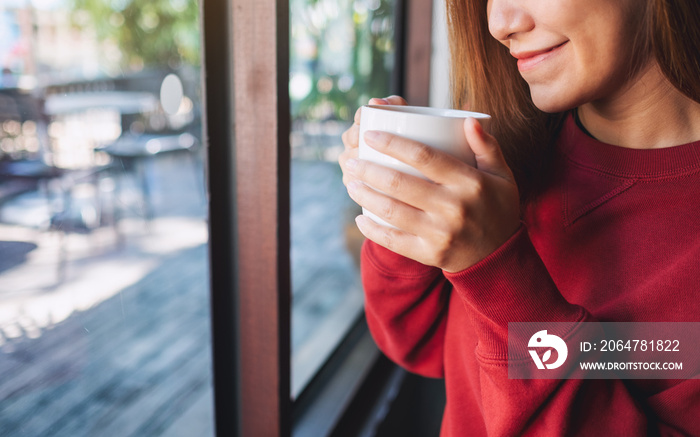 Closeup image of a young woman holding and drinking hot coffee