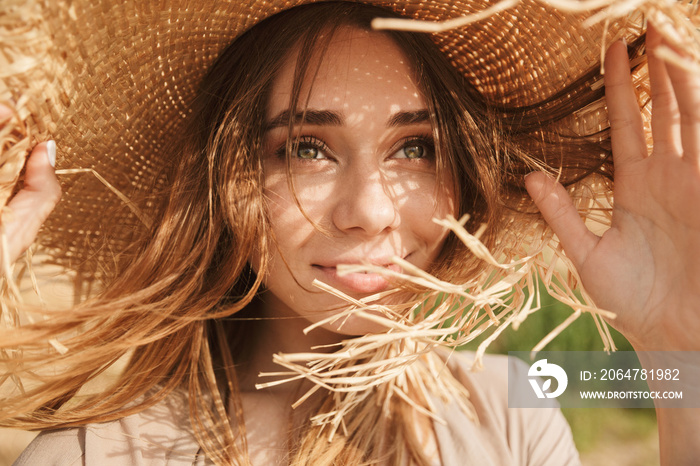 Optimistic smiling gorgeous beautiful woman posing outdoors at the sea beach wearing hat.