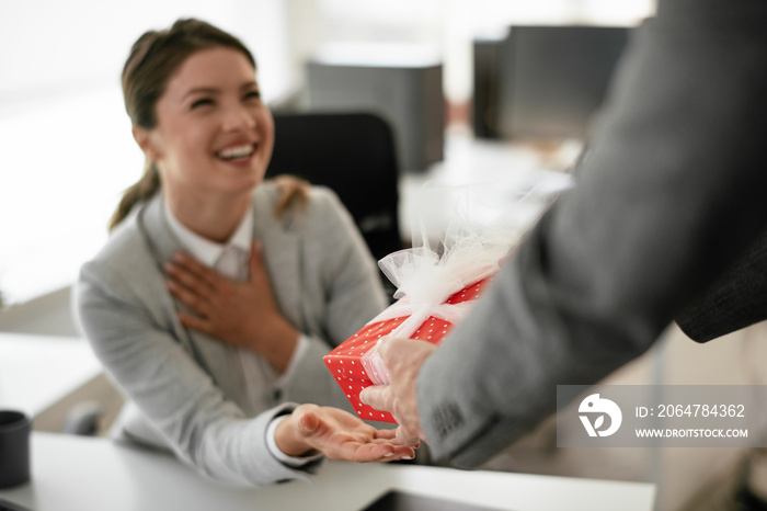 Young businessman giving his colleague present in office. Young man suprise beautiful businesswoman 