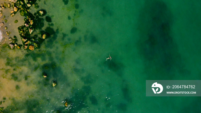 Aerial view of a girl swimming in sea with Algae green water by the rocky beach. Coast of sea in sum