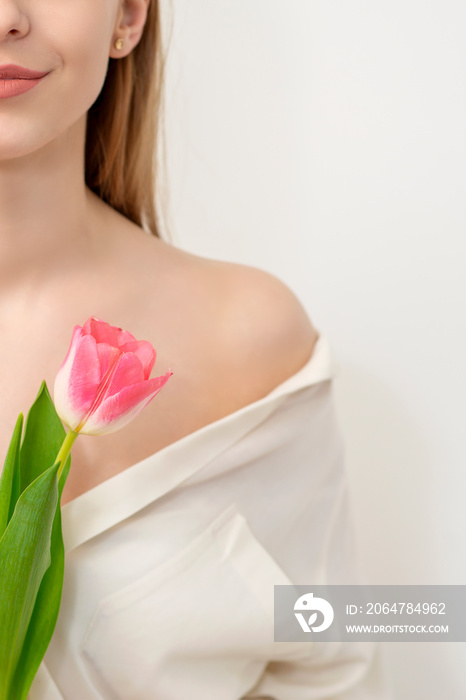 Half face of a beautiful caucasian young woman with one tulip against a white background