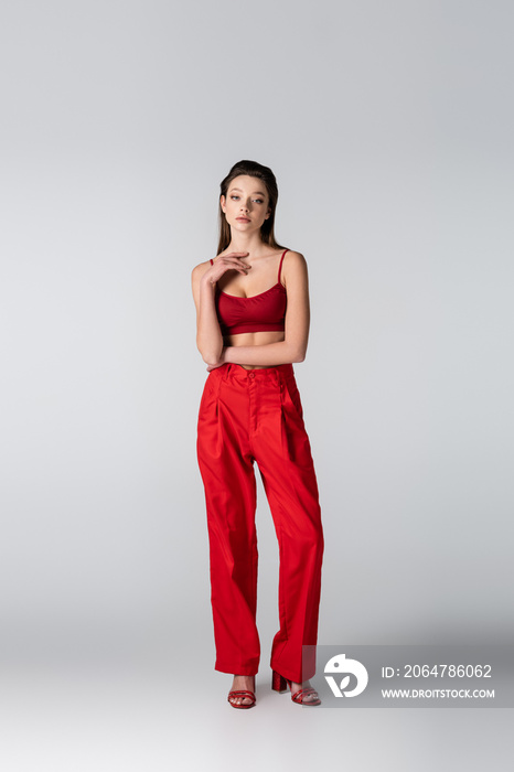 full length of model in red crop top and pants standing on grey.