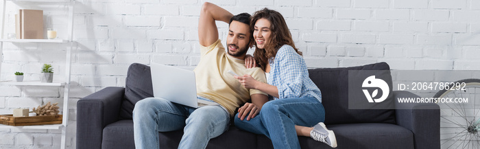 happy woman pointing at laptop near muslim boyfriend, banner.