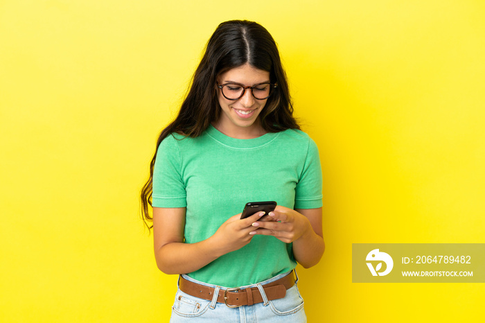 Young caucasian woman isolated on yellow background sending a message with the mobile