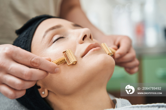 Cosmetician massaging the client face with acupressure metal roller massagers