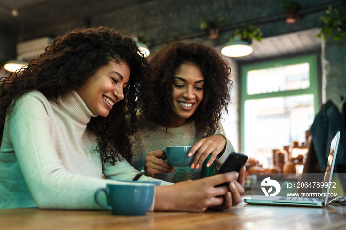 Close up of two happy african girlfriends sitting at the cafe