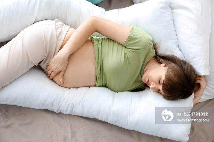 Young pregnant woman sleeping on maternity pillow at home