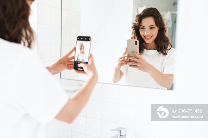 Photo of woman taking selfie on cellphone while looking at mirror