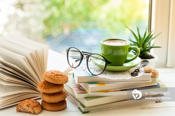 咖啡杯、打开的书、玻璃杯、饼干和窗户上的花。阅读和早餐。海螺