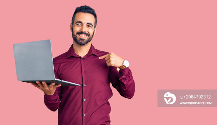 年轻的西班牙男子拿着笔记本电脑，指着一个微笑的自己，快乐而自豪